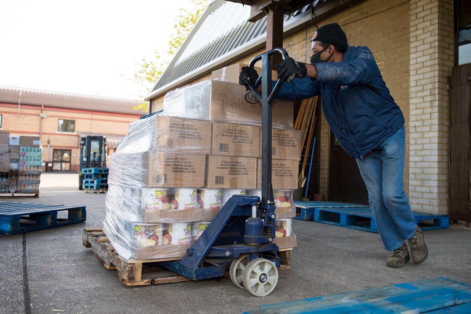 A warehouse worker pulling a pallet of boxed stock with a hand truck